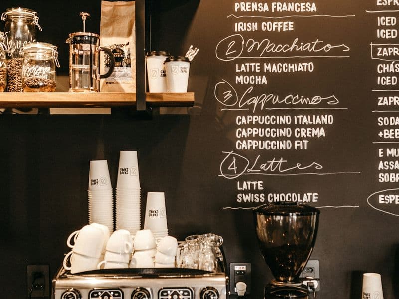 Pizarra negra con la carta de cafés escrita a mano, sobre la máquina de espresso