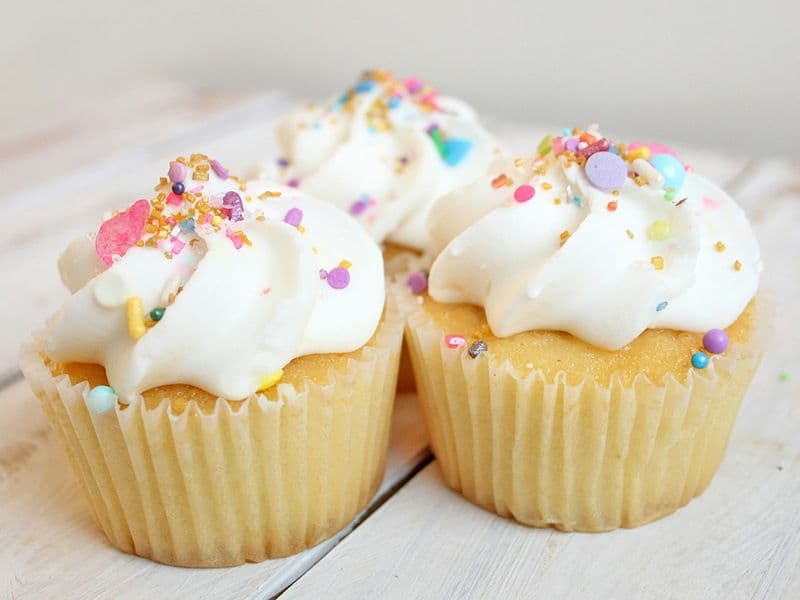 Tres cupcakes con crema blanca y grageas de colores sobre madera clara