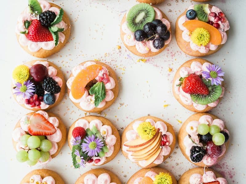 Tartaletas con crema rosada decoradas con frutas y flores vistas desde arriba