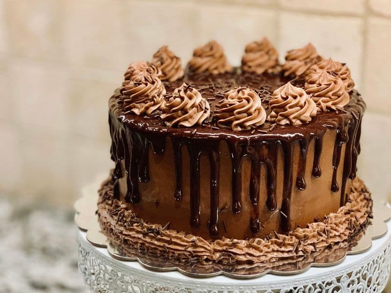 Torta de chocolate con ganache escurrido y rosetones de crema sobre un pedestal