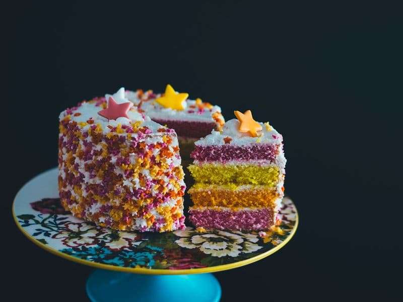 Torta de capas de colores decorada con grageas y estrellas, con una porción cortada